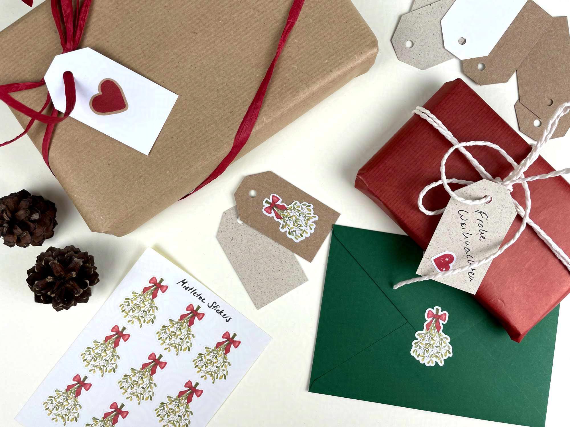Verpackte Geschenke, ein weihnachtlich dekorierter Brief, Geschenkanhänger und Mistelzweig-Aufkleber liegen auf einem Tisch.