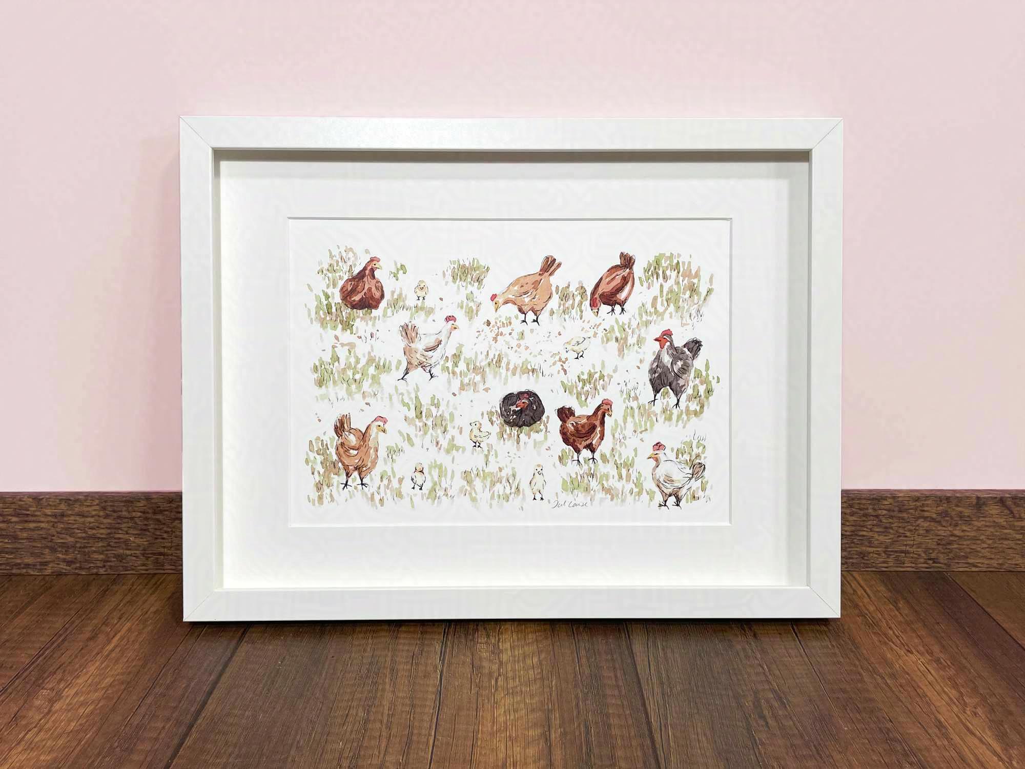 Ein Poster in einem weißen Bilderrahmen steht auf einem Holzfußboden an eine hellrosa Wand gelehnt. Das Poster zeigt eine Aquarell- und Tusche-Zeichnung von Hühnern auf einer Wiese.
