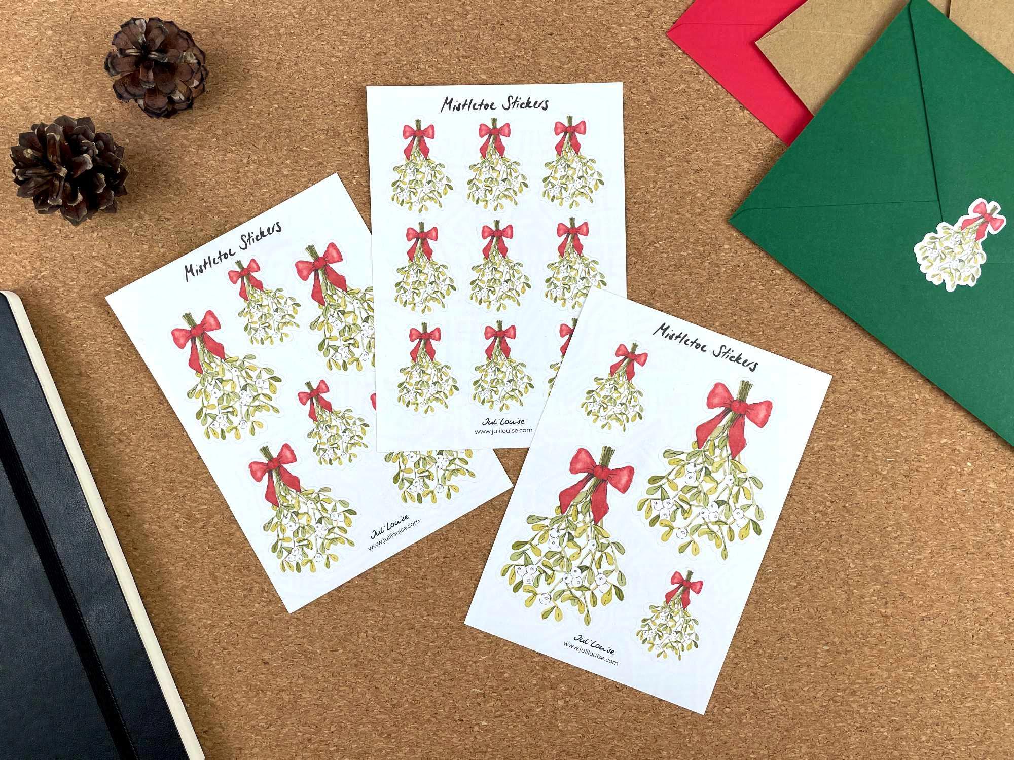 Drei Stickerbögen liegen auf einem Tisch. Die Stickerbögen enthalten Mistelzweig-Aufkleber in unterschiedlichen Größen.