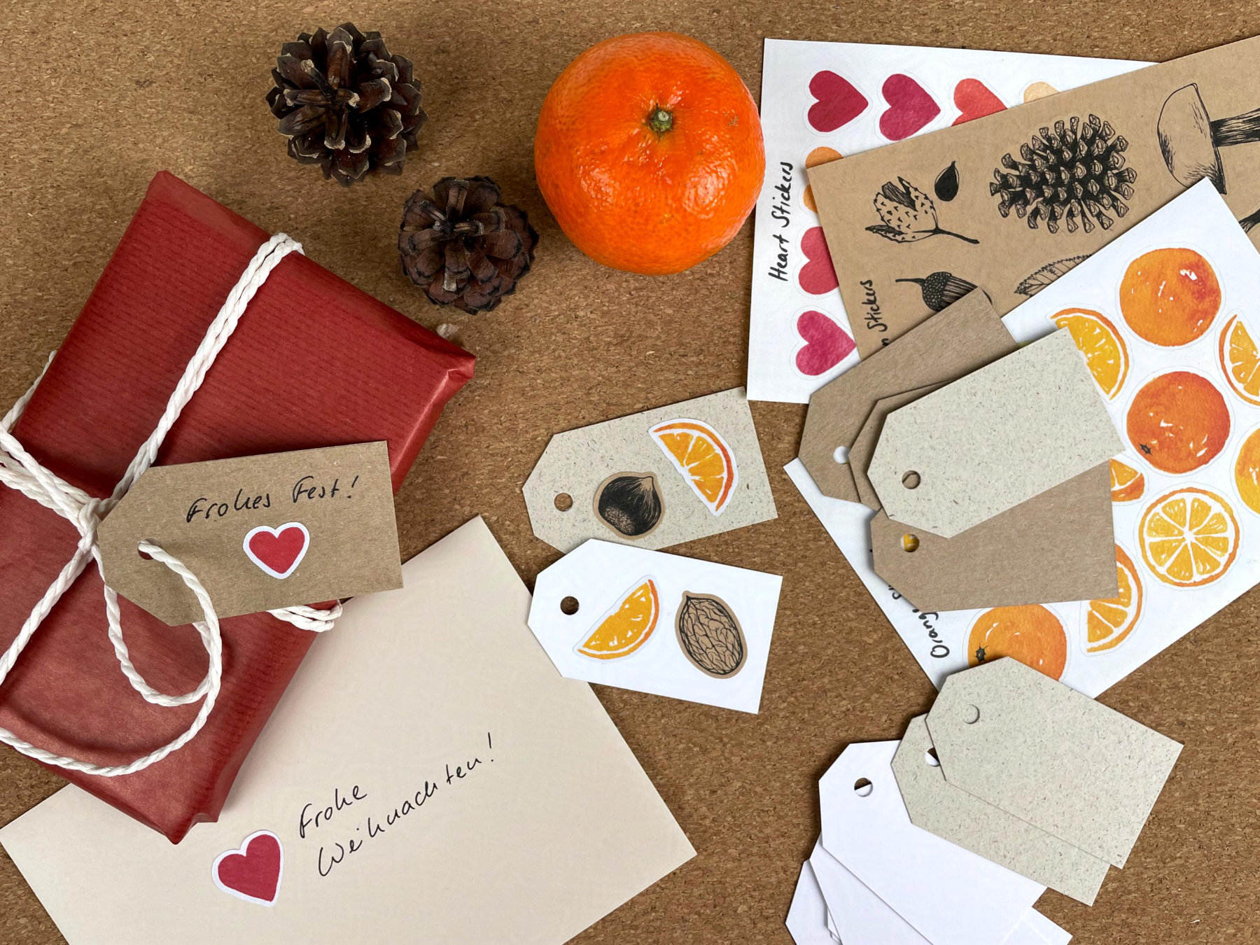 Eingepackte Geschenke, Geschenkanhänger, Stickerbögen und Weihnachtspost liegen auf einem Tisch. Ein Brief und mehrere Geschenkanhänger wurden mit illustrierten Stickern dekoriert.