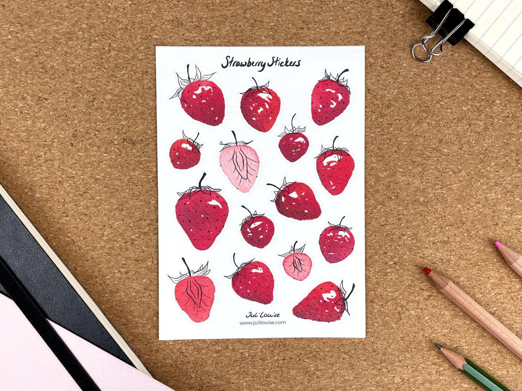 Ein Stickerbogen mit Erdbeerstickern liegt auf einem Tisch. Die Sticker zeigen ganze sowie aufgeschnittene Erdbeeren. Die Erdbeeren wurden mit Aquarellfarben gemalt.